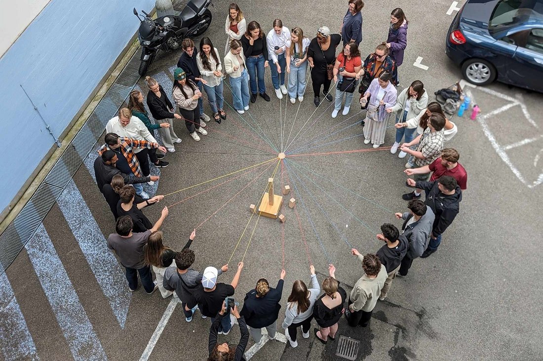 Die am Planspiel Teilnehmenden stehen im Kreis, wobei jede Person eine Schnur hält, die in der Mitte des Kreises zusammengeführt werden. 