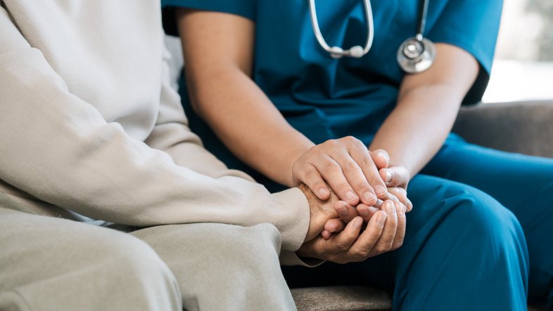 Eine Krankenschwester hält die Hand einer Patientin.