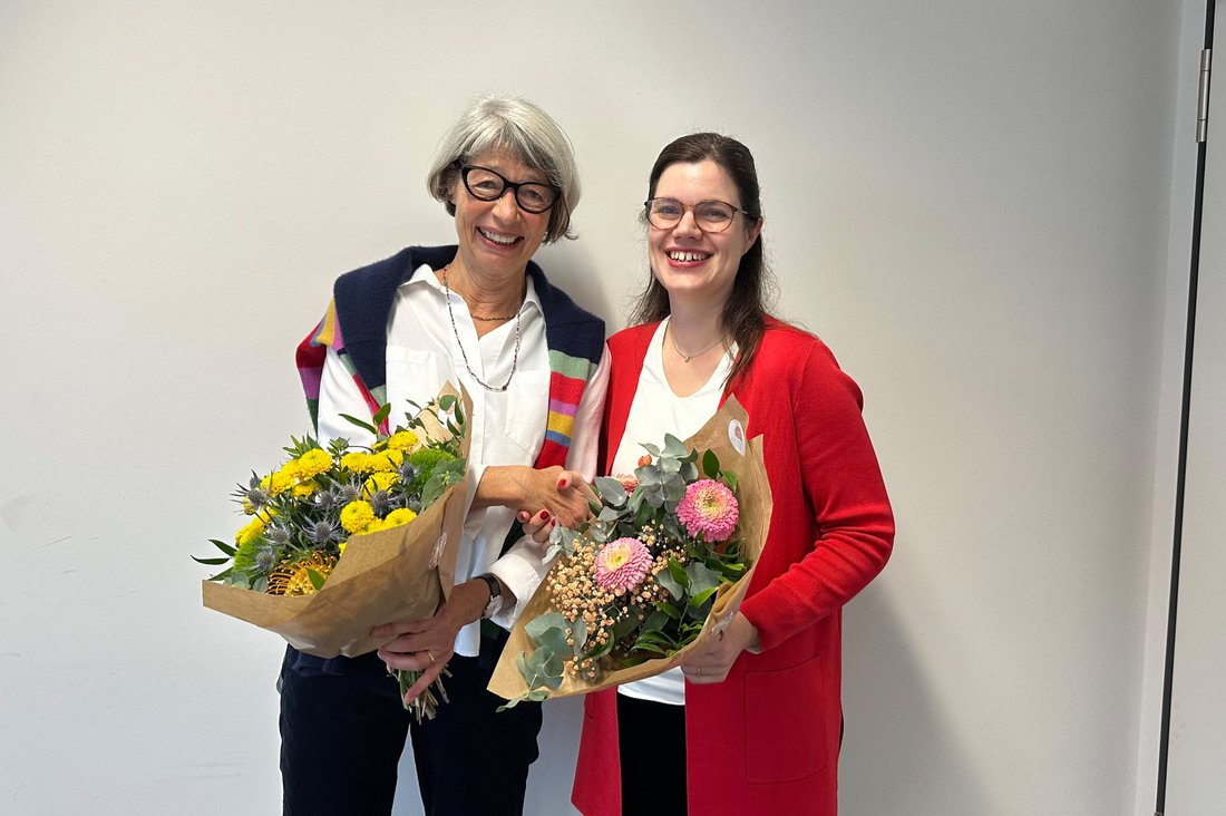 Prof.in Dr. Andrea Steinhilber (l.) und Prof.in Dr. Monika Mages-Maurer stehen nebeneinander, beide mit einem Blumenstrauß in der Hand. 