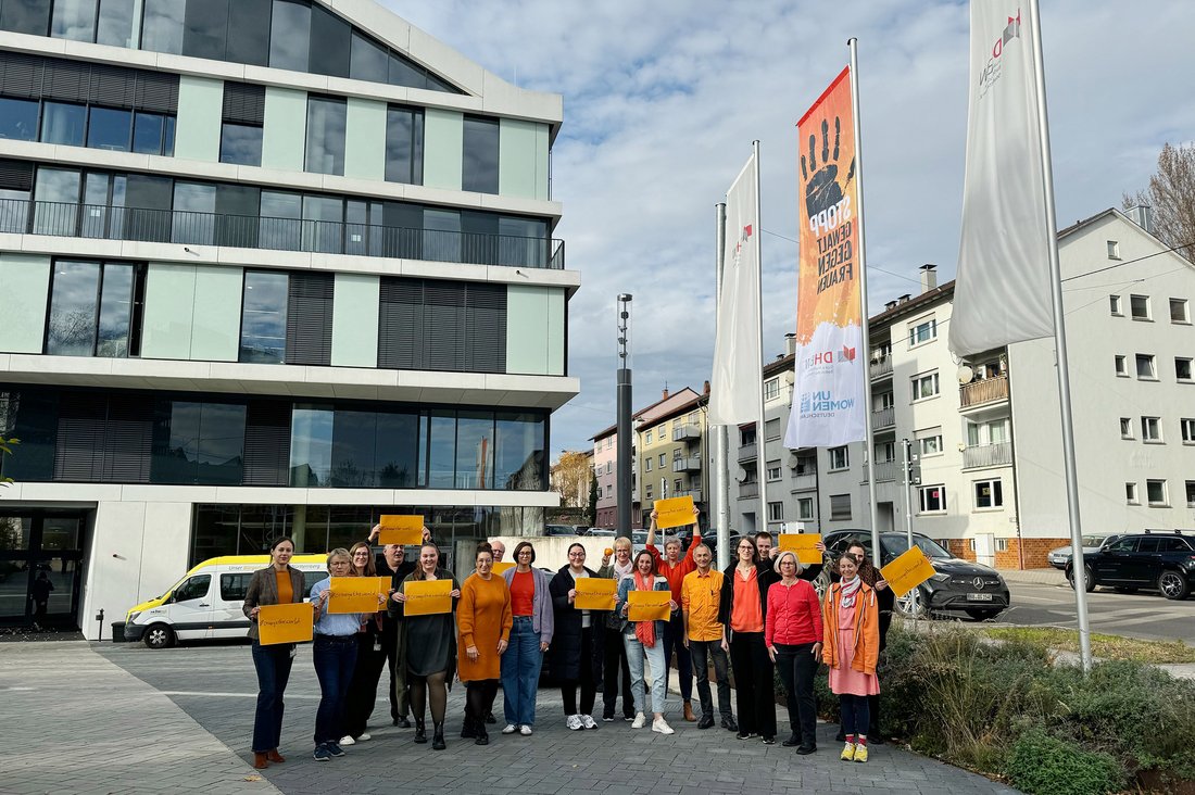 Mitarbeitende der DHBW Stuttgart vor der Flagge der UN-Kampagne „Orange the World“ am Internationalen Tag zur Beendigung der Gewalt an Frauen