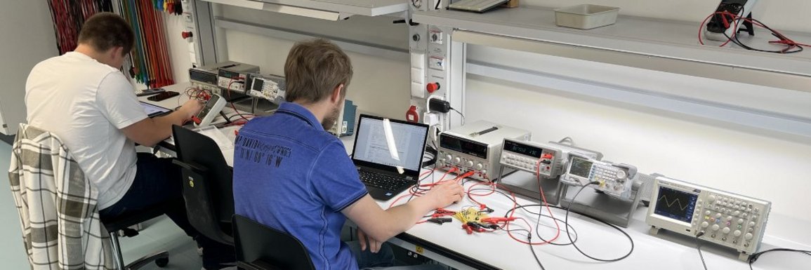 Im Labor Grundlagen der Elektrotechnik führen 2 Studierende Versuche durch. Blick über die Schulter auf die Versuchsanordnung.