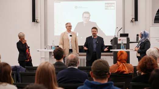 Podiumsdiskussion - Mehrere Personen stehen auf der Bühne und sprechen.