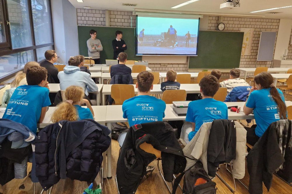 Gruppenbild - Schülerinnen und Schüler sitzen in einem Vortragsraum und folgen einer Präsentation auf der Leinwand vor ihnen.