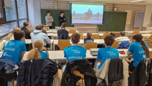 Gruppenbild - Schülerinnen und Schüler sitzen in einem Vortragsraum und folgen einer Präsentation auf der Leinwand vor ihnen.